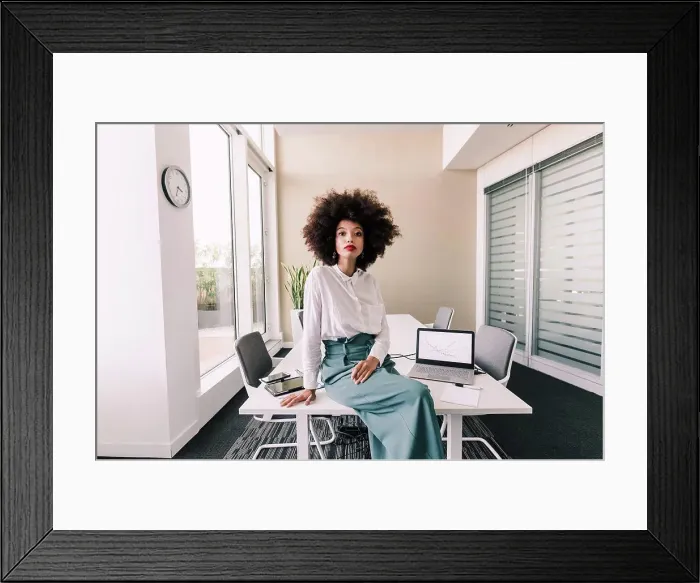 Framed Print : Portrait of businesswoman sitting on desk in office Framed Print : Portrait of businesswoman sitting on desk in office