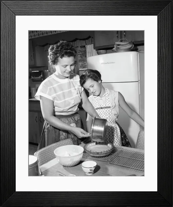 Framed Print : Mid adult woman preparing food with her daughter standing beside her Framed Print : Mid adult woman preparing food with her daughter standing beside her