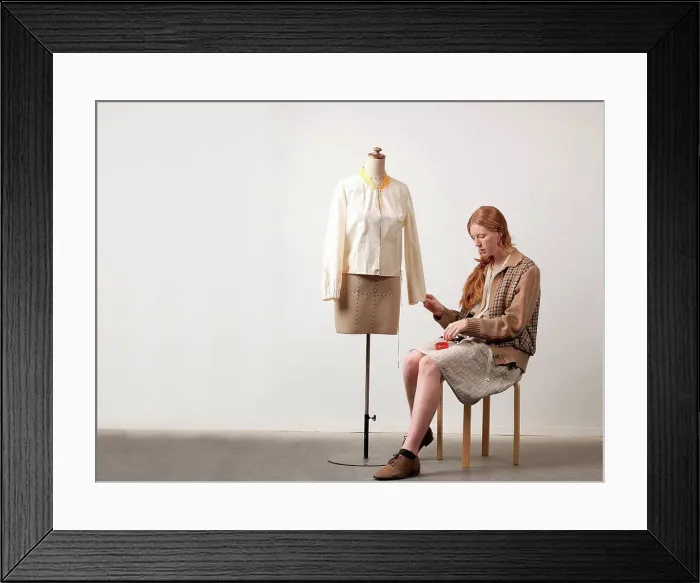 Framed Print : Young female fashion designer sitting on stool pinning blouse on dressmaker's dummy Framed Print : Young female fashion designer sitting on stool pinning blouse on dressmaker's dummy
