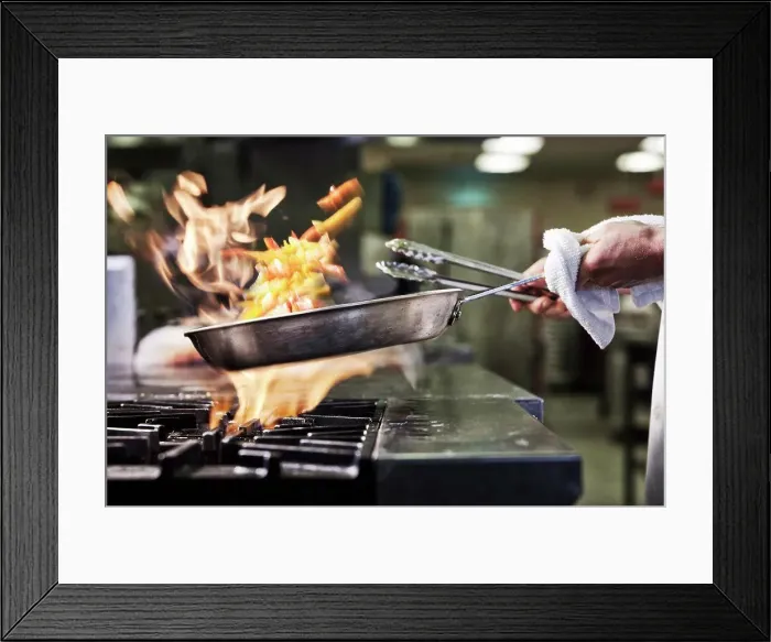 Framed Print : Close-up of chef's hands holding a sauté pan to cook food, flambéing contents. Flames rising from the pan Framed Print : Close-up of chef's hands holding a sauté pan to cook food, flambéing contents. Flames rising from the pan