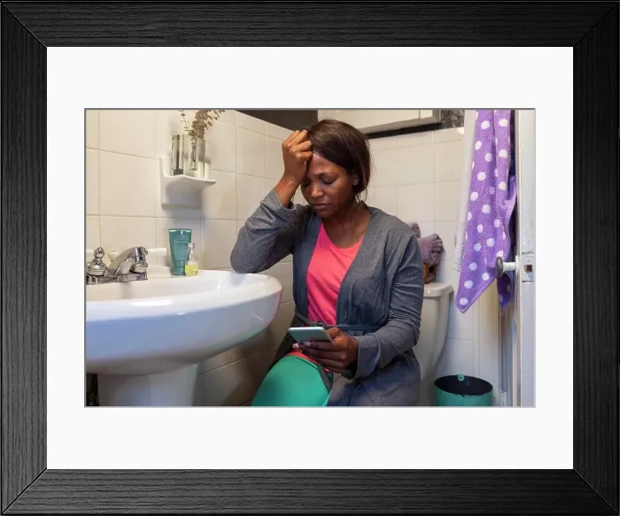 Framed Print : Young woman in the bathroom feeling ill using Tele-medicine to communicate with a doctor