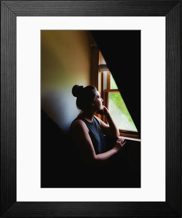 Framed Print : Woman looking out of a window in a dark room in the daytime Framed Print : Woman looking out of a window in a dark room in the daytime
