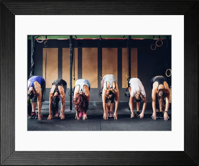 Framed Print : Row of women training in gym, bending forward touching floor