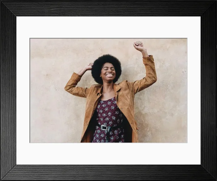 Framed Print : Young woman with afro hair feeling excited against stone wall Framed Print : Young woman with afro hair feeling excited against stone wall