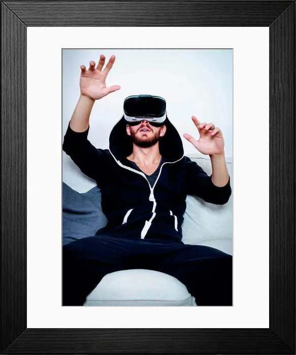 Framed Print : Mid adult man on sofa with arms raised watching virtual reality headset