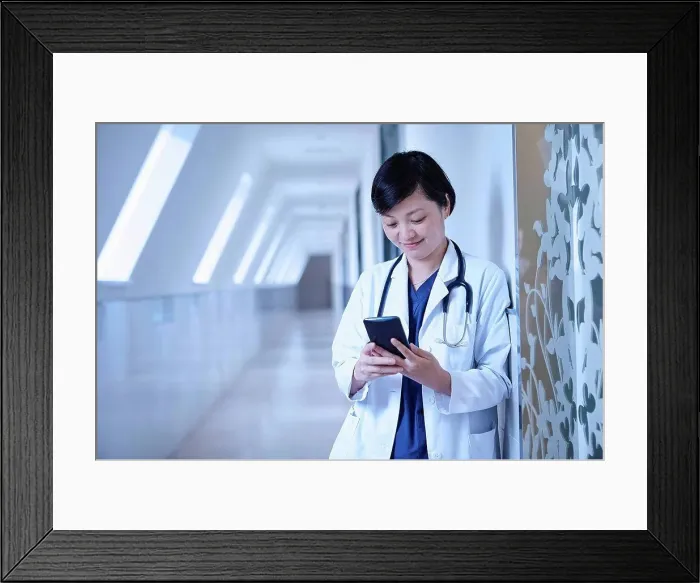 Framed Print : Doctor in hospital corridor leaning against wall using smartphone Framed Print : Doctor in hospital corridor leaning against wall using smartphone