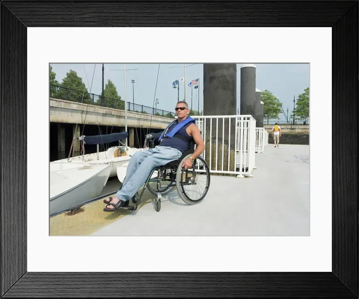 Framed Print : Mature man sitting in a wheelchair at a harbor for adaptive sailing Framed Print : Mature man sitting in a wheelchair at a harbor for adaptive sailing