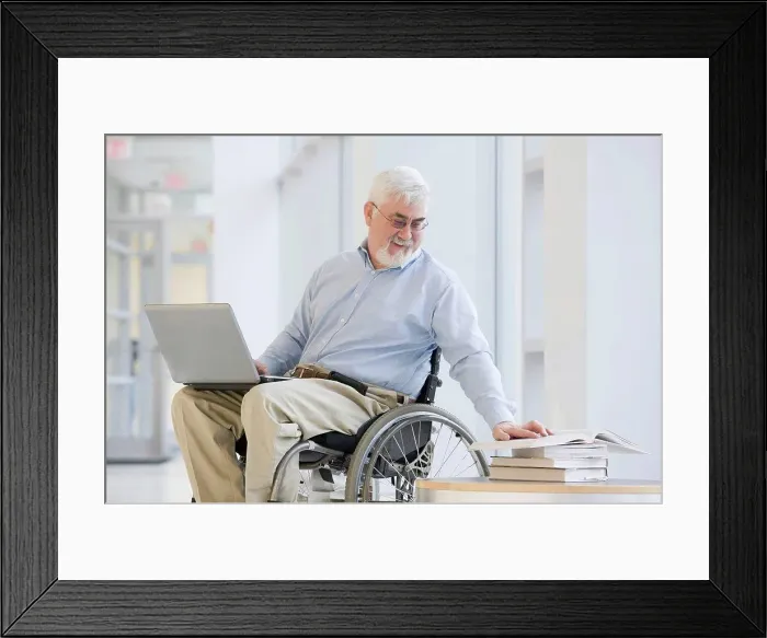 Framed Print : University professor with Muscular Dystrophy reading a book and using a laptop Framed Print : University professor with Muscular Dystrophy reading a book and using a laptop