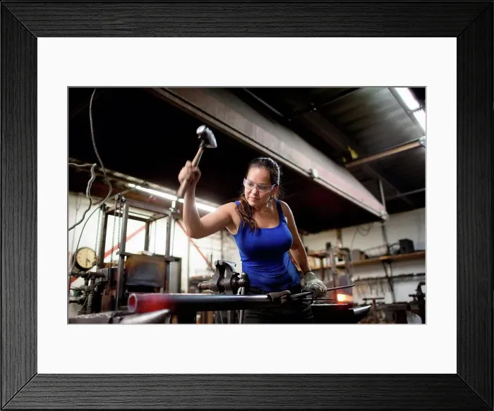 Framed Print : Female metalsmith hammering red hot metal rod on workshop anvil