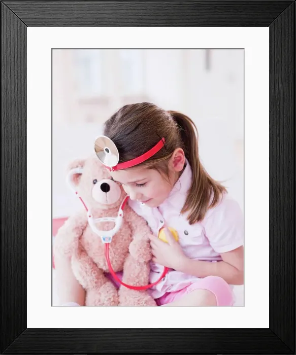 Framed Print : A young girl in a light pink shirt and toy medic attire playing with her teddy bear Framed Print : A young girl in a light pink shirt and toy medic attire playing with her teddy bear