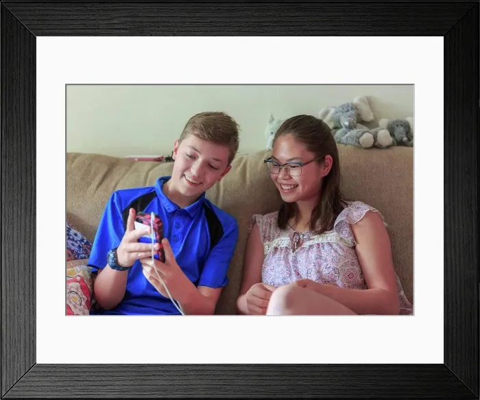 Framed Print : Teenage girl who has Learning Disability looking at phone with her brother