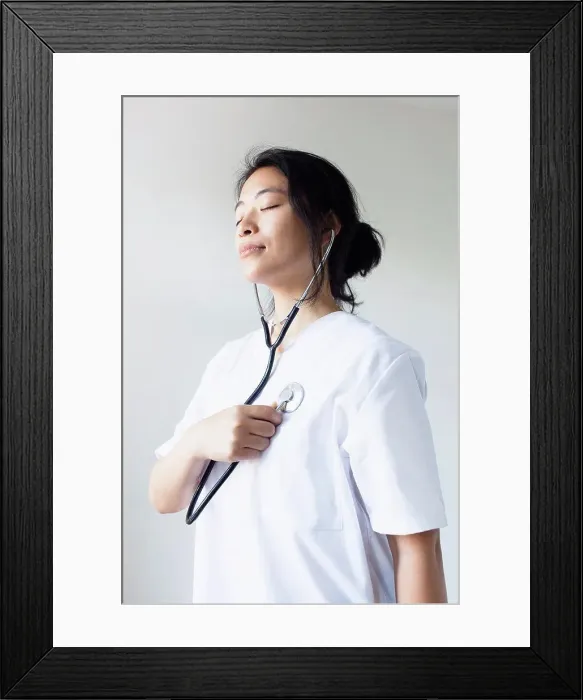 Framed Print : Female doctor listening self heart beat with stethoscope against wall Framed Print : Female doctor listening self heart beat with stethoscope against wall
