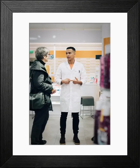 Framed Print : Full length of male pharmacist talking with senior female customer in medical store