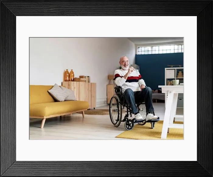 Framed Print : Smiling senior freelancer on wheelchair in living room Framed Print : Smiling senior freelancer on wheelchair in living room