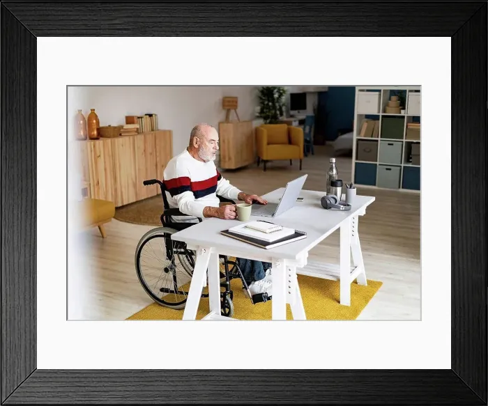 Framed Print : Senior businessman on wheelchair with coffee mug using laptop at home office