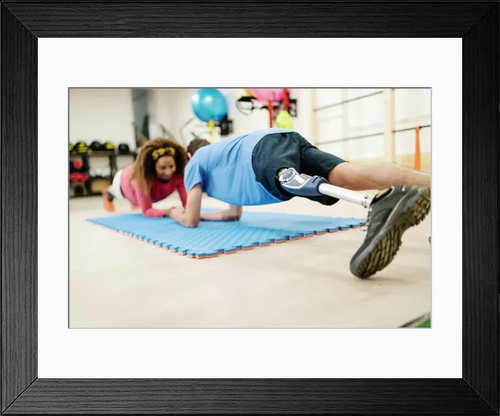 Framed Print : Sportsman with disability practicing plank position with friend on mat in gym Framed Print : Sportsman with disability practicing plank position with friend on mat in gym