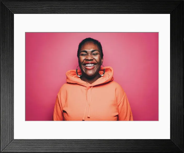 Framed Print : Cheerful mid adult woman wearing orange hooded shirt over pink background Framed Print : Cheerful mid adult woman wearing orange hooded shirt over pink background