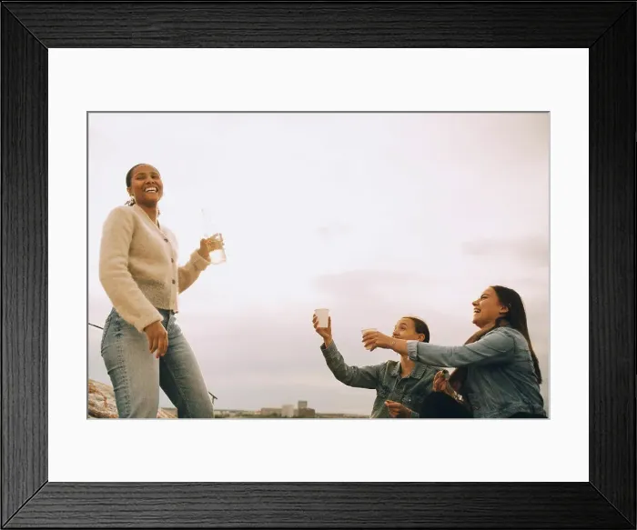 Framed Print : Happy woman giving drink to female friends against sky during picnic Framed Print : Happy woman giving drink to female friends against sky during picnic
