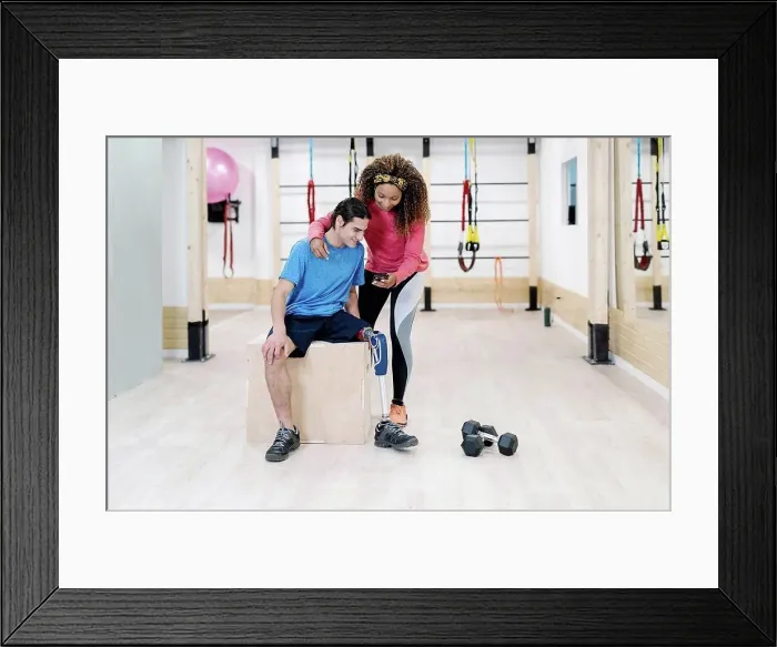 Framed Print : Athlete sharing mobile phone with disabled friend in gym Framed Print : Athlete sharing mobile phone with disabled friend in gym