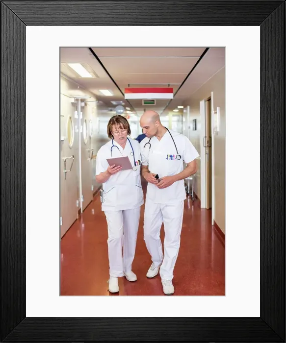 Framed Print : Male and female doctors using digital tablet while walking in hospital corridor