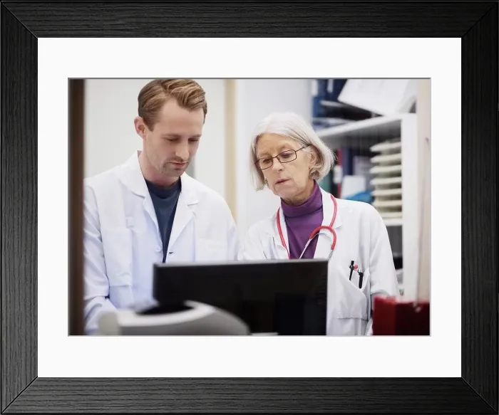 Framed Print : Senior female doctor with male colleague using computer in examination room