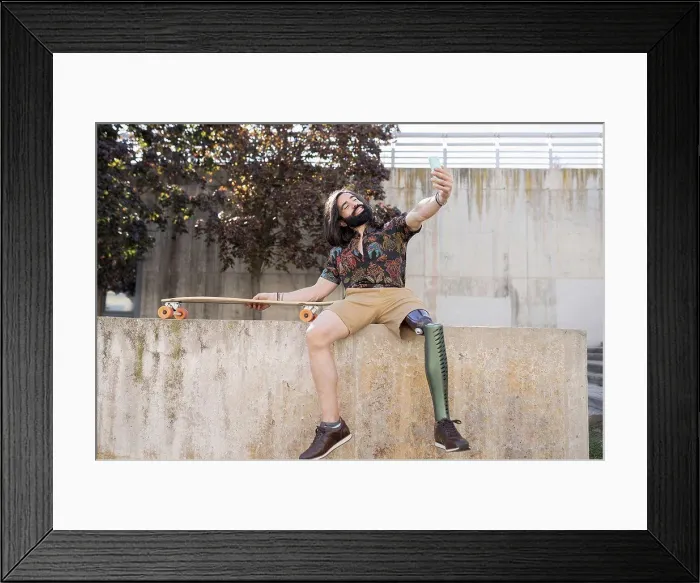 Framed Print : Smiling man with amputed leg taking selfie through smart phone on wall Framed Print : Smiling man with amputed leg taking selfie through smart phone on wall