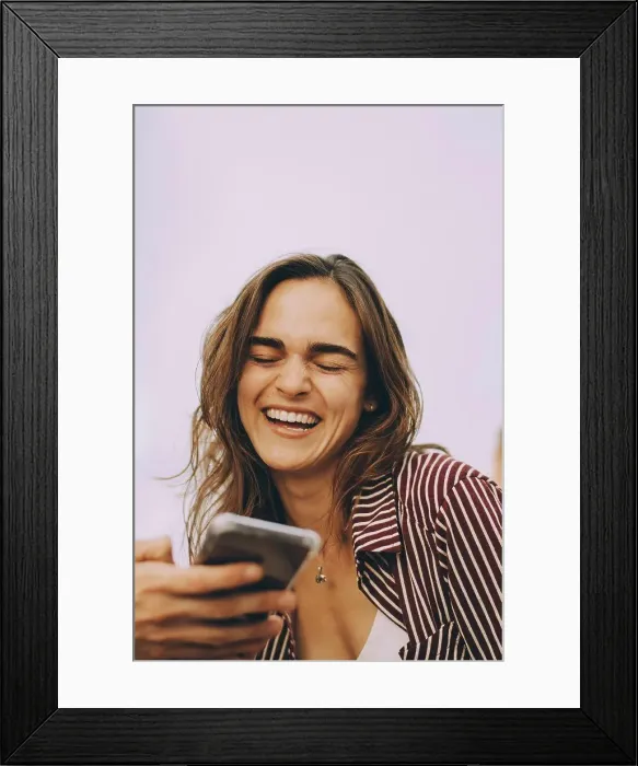 Framed Print : Cheerful young woman looking at smart phone held by friend at terrace Framed Print : Cheerful young woman looking at smart phone held by friend at terrace