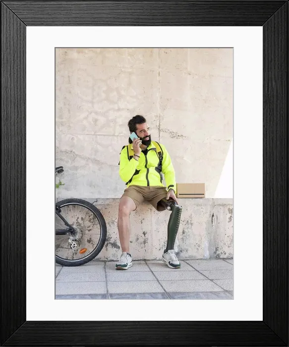 Framed Print : Delivery man with amputed leg talking on mobile phone in park Framed Print : Delivery man with amputed leg talking on mobile phone in park