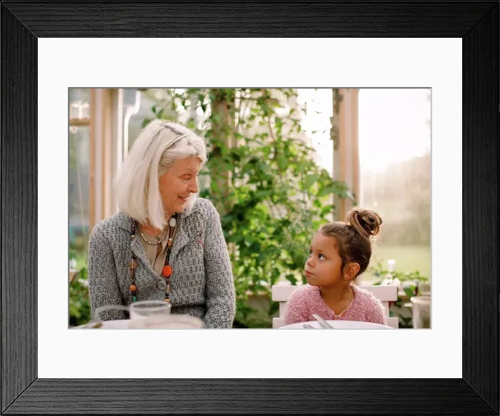 Framed Print : Smiling grandmother looking at granddaughter while having lunch Framed Print : Smiling grandmother looking at granddaughter while having lunch