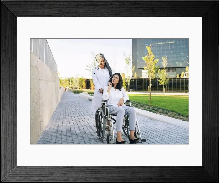 Framed Print : Disabled woman talking with female doctor pushing wheelchair on footpath