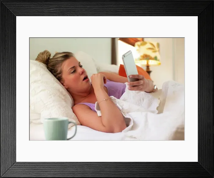 Framed Print : Coughing young woman in her bed with using smartphone to check in with doctor Framed Print : Coughing young woman in her bed with using smartphone to check in with doctor