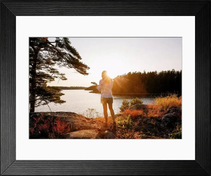 Framed Print : Rear view of woman holding mobile phone while standing on lakeshore at sunset Framed Print : Rear view of woman holding mobile phone while standing on lakeshore at sunset