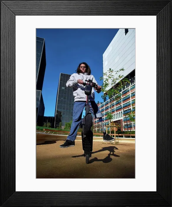 Framed Print : Young disabled man practicing stunt on electric push scooter in playground against buildings in city Framed Print : Young disabled man practicing stunt on electric push scooter in playground against buildings in city
