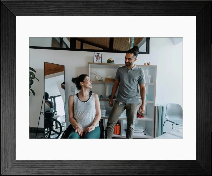 Framed Print : Smiling physiotherapist with female patient sitting on wheelchair in medical practice