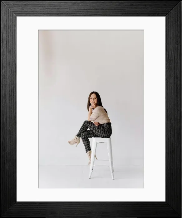 Framed Print : Studio shot of young woman sitting on stool Framed Print : Studio shot of young woman sitting on stool