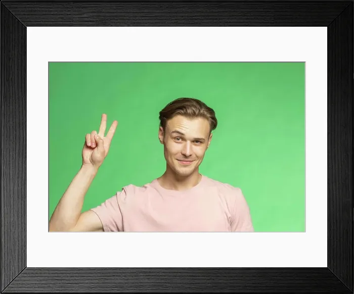 Framed Print : Portrait confident young man gesturing peace sign on green background Framed Print : Portrait confident young man gesturing peace sign on green background