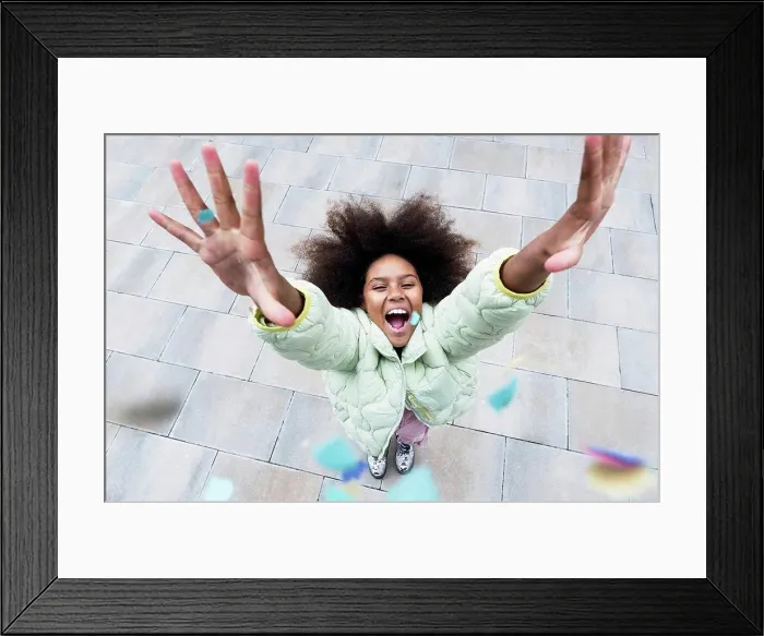 Framed Print : Cheerful girl with arms raised standing amidst confetti falling on footpath Framed Print : Cheerful girl with arms raised standing amidst confetti falling on footpath