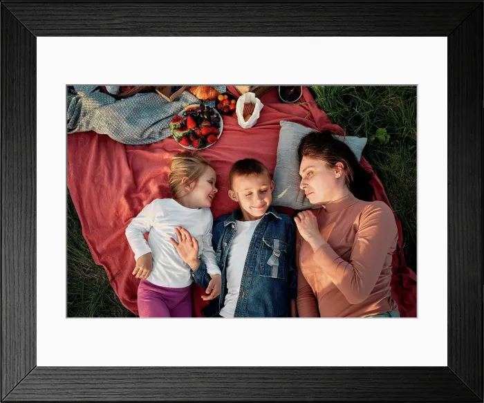 Framed Print : Mother looking at children lying on picnic blanket in field