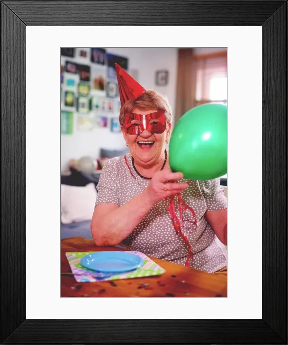 Framed Print : Senior woman waving balloons at birthday party Framed Print : Senior woman waving balloons at birthday party