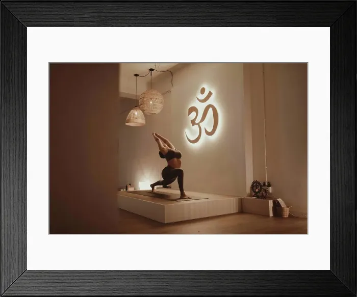 Framed Print : Female yoga instructor with arms raised bending while practicing by Om symbol