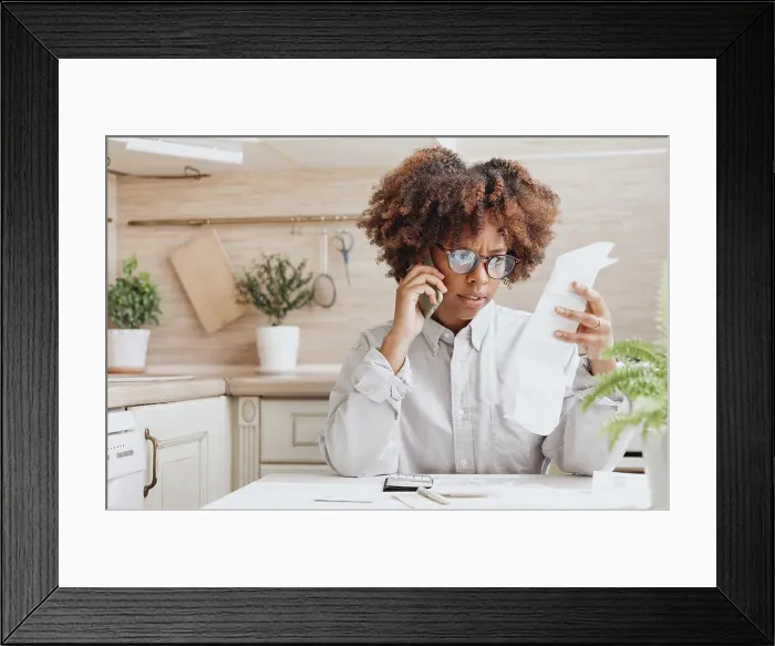 Framed Print : Woman talking on the phone looking bills for payment in the kitchen Framed Print : Woman talking on the phone looking bills for payment in the kitchen