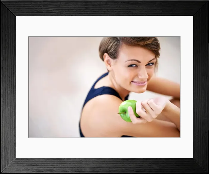 Framed Print : Building blocks for a happy healthy life. a sporty young woman sitting on a gym floor eating an apple