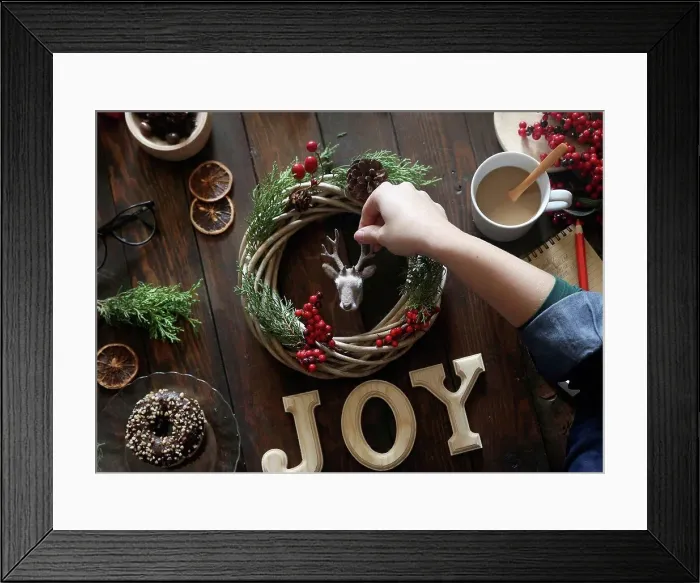 Framed Print : Woman's hand decorating Christmas wreath on wooden table