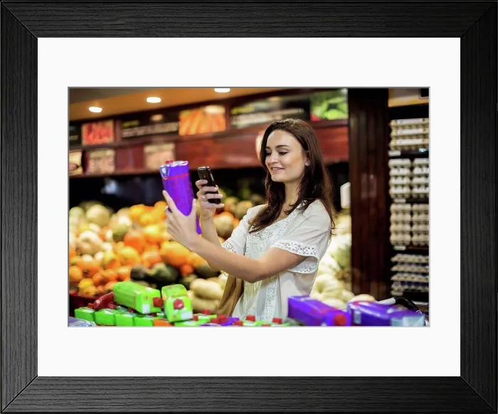 Framed Print : Woman at supermarket scanning prices with her smart phone Framed Print : Woman at supermarket scanning prices with her smart phone