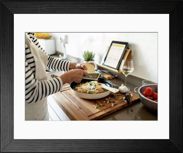 Framed Print : Close-up of woman with tablet cooking pasta dish in kitchen at home Framed Print : Close-up of woman with tablet cooking pasta dish in kitchen at home