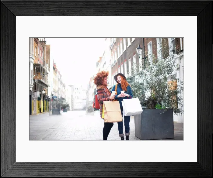 Framed Print : Two young women standing in street, holding shopping bags and coffee cup