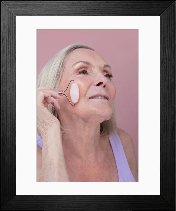 Framed Print : Studio shot of senior woman using face roller Framed Print : Studio shot of senior woman using face roller