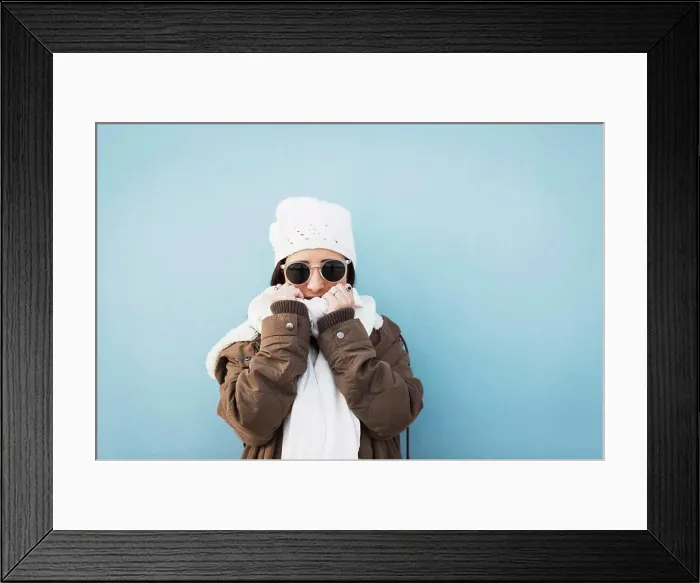 Framed Print : Fashionable woman wearing warm clothing standing against blue background Framed Print : Fashionable woman wearing warm clothing standing against blue background
