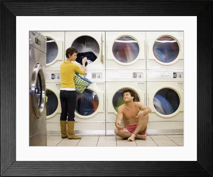 Framed Print : Man in boxers sleeping at Laundromat with woman removing clothing from dryer Framed Print : Man in boxers sleeping at Laundromat with woman removing clothing from dryer