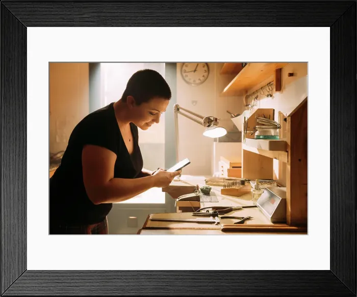 Framed Print : Smiling female craftsperson taking photo of ring with mobile phone at workshop Framed Print : Smiling female craftsperson taking photo of ring with mobile phone at workshop